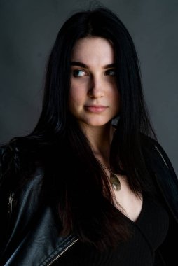 Karanlık stüdyoda şık giyinmiş esmer bir kadın poz veriyor.  