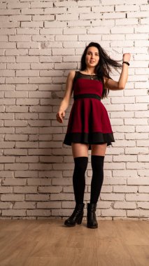 Koyu renk saçlı, kırmızı elbiseli, karanlık stüdyoda poz veren genç ve seksi bir kadın..