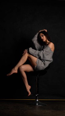 Stüdyoda siyah bir arka planda duran kolları olan güzel gri elbiseli seksi bir genç. 