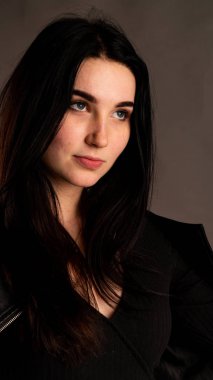 Karanlık stüdyoda şık giyinmiş esmer bir kadın poz veriyor.  