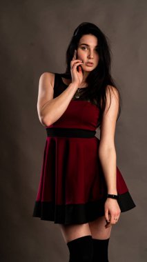 Koyu renk saçlı, kırmızı elbiseli, karanlık stüdyoda poz veren genç ve seksi bir kadın..