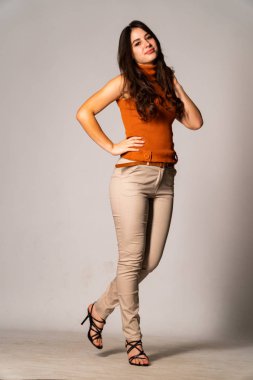 Güzel esmer manken şık kıyafetler içinde, aydınlık odada poz veriyor. 