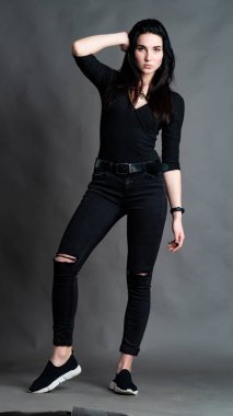 Yüksek tahta koltukta bacak bacak üstüne atmış esmer bir kadının portresi. Geniş paçalı pantolon giyen şık bir kız. Gri arkaplanda stüdyo çekimi