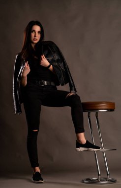 Karanlık stüdyoda şık giyinmiş esmer bir kadın poz veriyor.  