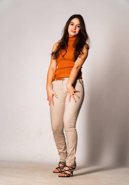 Güzel esmer manken şık kıyafetler içinde, aydınlık odada poz veriyor. 