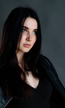 Karanlık stüdyoda şık giyinmiş esmer bir kadın poz veriyor.  