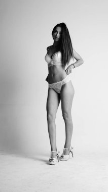 Beyaz iç çamaşırlı ve yüksek topuklu bir kız beyaz arka planda poz veriyor.. 