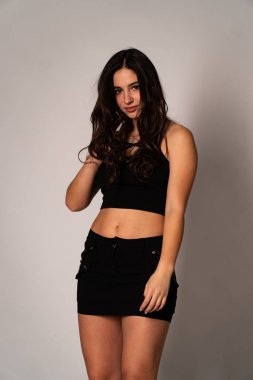 Siyah elbiseli, siyah saçlı, açık renk stüdyo arka planında poz veren güzel bir kadın. 