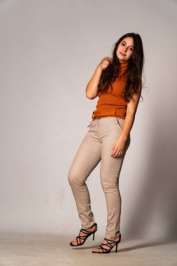 Güzel esmer manken şık kıyafetler içinde, aydınlık odada poz veriyor. 