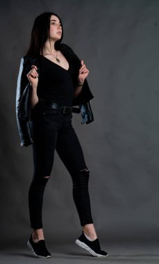 Karanlık stüdyoda şık giyinmiş esmer bir kadın poz veriyor.  