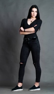 Yüksek tahta koltukta bacak bacak üstüne atmış esmer bir kadının portresi. Geniş paçalı pantolon giyen şık bir kız. Gri arkaplanda stüdyo çekimi