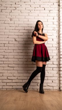 Koyu renk saçlı, kırmızı elbiseli, karanlık stüdyoda poz veren genç ve seksi bir kadın..