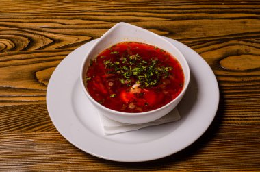 Çorba, ekşi kremalı borç, arka planda boncuk ve turşu. Borç beyaz bir tabakta, ekmek dilimleri ahşap bir kesme tahtasında, turşular ahşap bir tabakta..