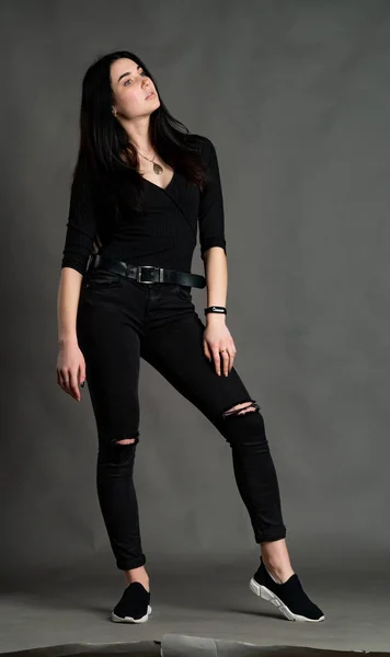 Retrato de una joven morenita sentada en una silla de madera con piernas cruzadas. Elegante y elegante chica con pantalones de pierna ancha. Estudio de rodaje sobre fondo gris — Foto de Stock