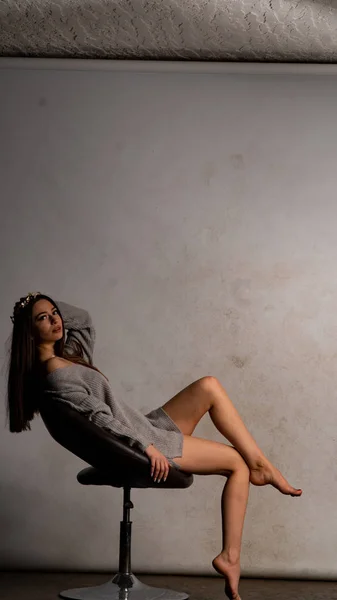 Beautiful sexy girl, posing a short gray dress, a white background chair — Stock Photo, Image