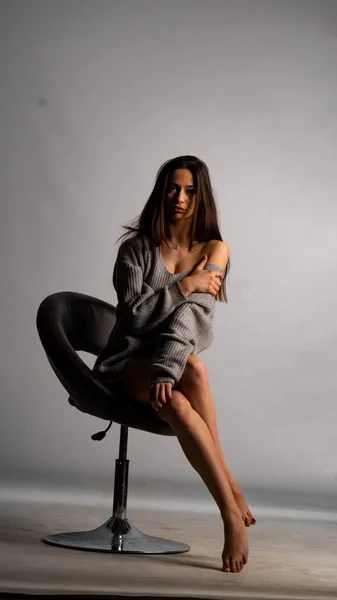 Mooi sexy meisje, poseren een korte grijze jurk, een witte achtergrond stoel — Stockfoto