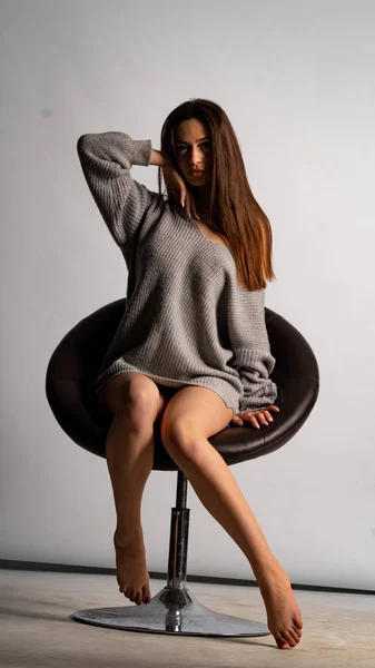 Hermosa chica sexy, con un vestido gris corto, una silla de fondo blanca. —  Fotos de Stock