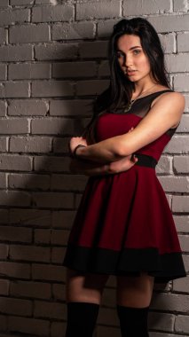 Koyu renk saçlı, kırmızı elbiseli, karanlık stüdyoda poz veren genç ve seksi bir kadın..