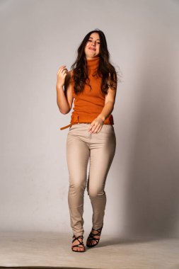 Güzel esmer manken şık kıyafetler içinde, aydınlık odada poz veriyor. 