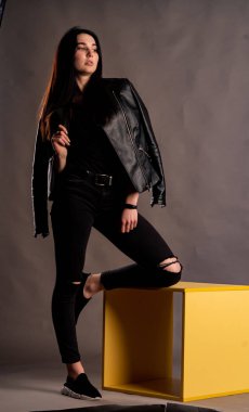 Karanlık stüdyoda şık giyinmiş esmer bir kadın poz veriyor.  