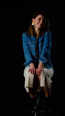 Siyah deri ceket giyen, siyah bluzlu, kısa etekli ve siyah arka planda poz veren güzel bir kadın. Siyah arka planda sarışın bir kadının stüdyo fotoğrafı.