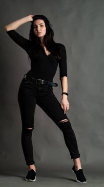 Yüksek tahta koltukta bacak bacak üstüne atmış esmer bir kadının portresi. Geniş paçalı pantolon giyen şık bir kız. Gri arkaplanda stüdyo çekimi