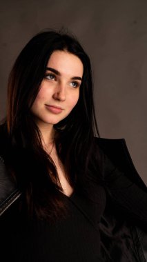 Karanlık stüdyoda şık giyinmiş esmer bir kadın poz veriyor.  