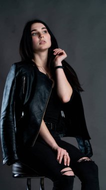 Karanlık stüdyoda şık giyinmiş esmer bir kadın poz veriyor.  