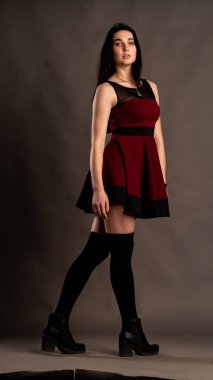 Karanlık stüdyoda şık giyinmiş esmer bir kadın poz veriyor.  