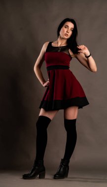 Karanlık stüdyoda şık giyinmiş esmer bir kadın poz veriyor.  