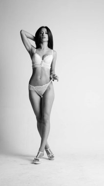 Beyaz iç çamaşırlı ve yüksek topuklu bir kız beyaz arka planda poz veriyor.. 