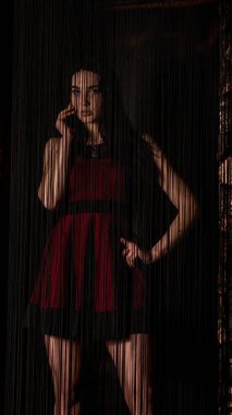 Koyu renk saçlı, kırmızı elbiseli, karanlık stüdyoda poz veren genç ve seksi bir kadın..