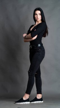 Yüksek tahta koltukta bacak bacak üstüne atmış esmer bir kadının portresi. Geniş paçalı pantolon giyen şık bir kız. Gri arkaplanda stüdyo çekimi