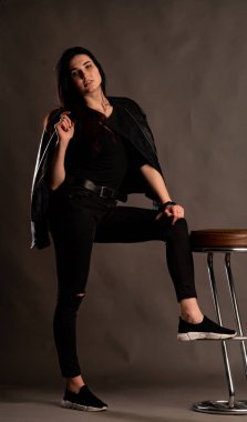 Karanlık stüdyoda şık giyinmiş esmer bir kadın poz veriyor.  