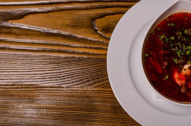 Çorba, ekşi kremalı borç, arka planda boncuk ve turşu. Borç beyaz bir tabakta, ekmek dilimleri ahşap bir kesme tahtasında, turşular ahşap bir tabakta..