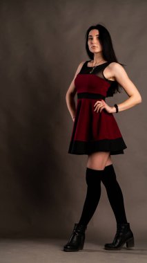 Karanlık stüdyoda şık giyinmiş esmer bir kadın poz veriyor.  