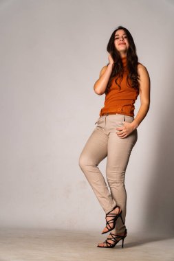 Güzel esmer manken şık kıyafetler içinde, aydınlık odada poz veriyor. 