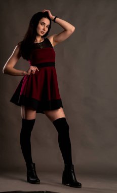 Karanlık stüdyoda şık giyinmiş esmer bir kadın poz veriyor.  