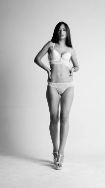 Beyaz iç çamaşırlı ve yüksek topuklu bir kız beyaz arka planda poz veriyor.. 