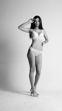 Beyaz iç çamaşırlı ve yüksek topuklu bir kız beyaz arka planda poz veriyor.. 