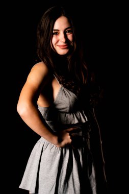 Koyu kahverengi saçlı, gri elbiseli, esmer, güzel bir kadın. Stüdyo arka planında poz veriyor.  