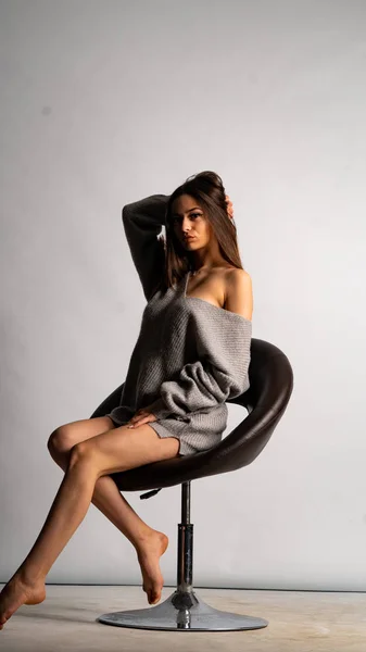 美しいセクシーな女の子が短いグレーのドレスと白い背景の椅子を着て — ストック写真