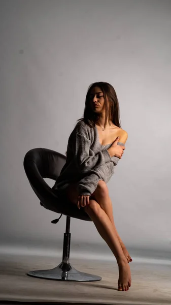Hermosa chica sexy, con un vestido gris corto, una silla de fondo blanca. — Foto de Stock