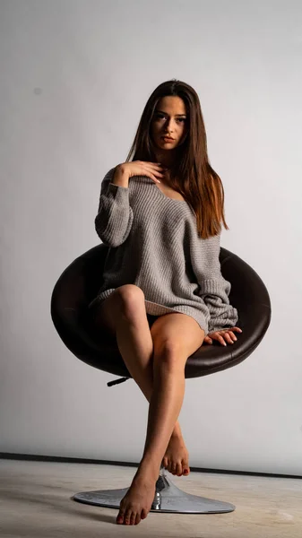 Красива сексуальна дівчина, позує коротку сіру сукню, білий стілець на фоні — стокове фото