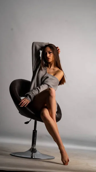 Hermosa chica sexy, con un vestido gris corto, una silla de fondo blanca. — Foto de Stock