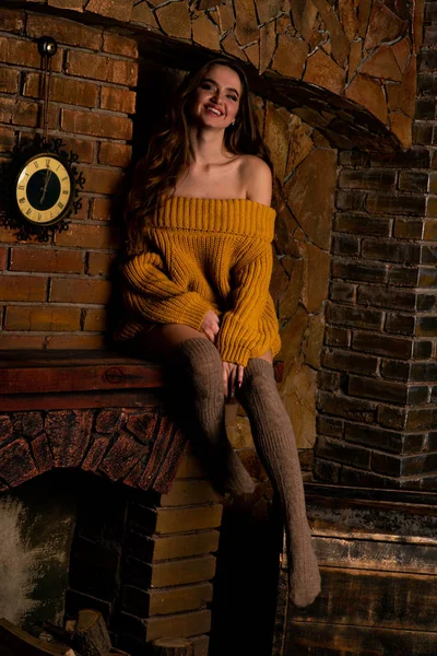 Hermosa chica sentada junto a la chimenea. Interior de lujo decorado para Navidad con ramas de abeto y juguetes —  Fotos de Stock