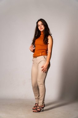 Güzel esmer manken şık kıyafetler içinde, aydınlık odada poz veriyor. 