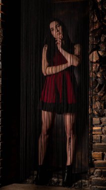 Koyu renk saçlı, kırmızı elbiseli, karanlık stüdyoda poz veren genç ve seksi bir kadın..