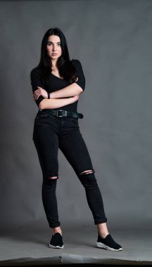 Yüksek tahta koltukta bacak bacak üstüne atmış esmer bir kadının portresi. Geniş paçalı pantolon giyen şık bir kız. Gri arkaplanda stüdyo çekimi