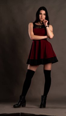 Karanlık stüdyoda şık giyinmiş esmer bir kadın poz veriyor.  